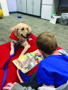 picture of a young buy reading to therapy dog, phoenix, on a mat at the library